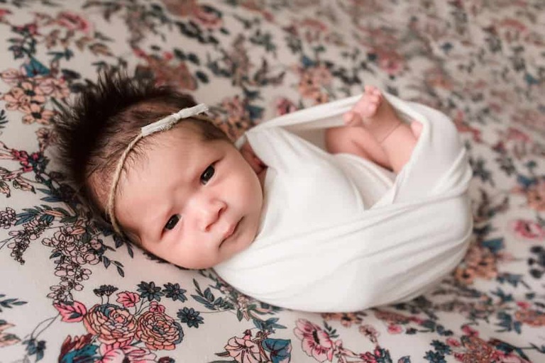 Newborn baby girl awake wrapped on floral backdrop.