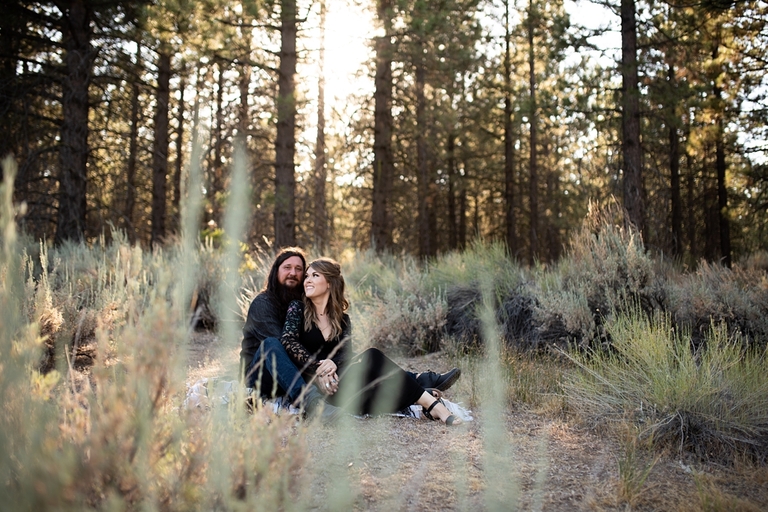 Couple sitting in front of forest embracing for engagement photos